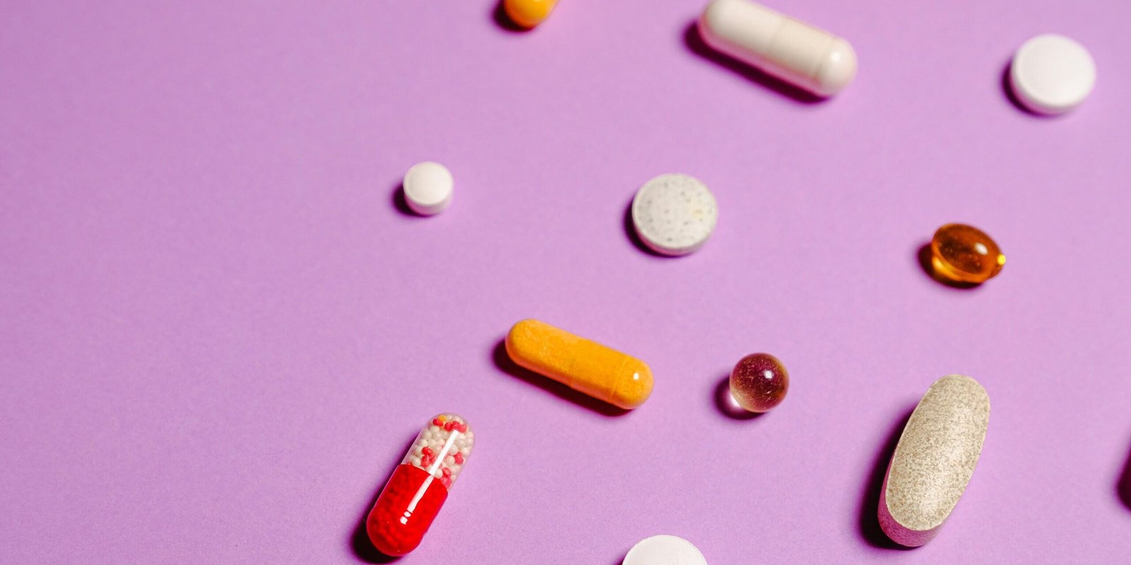 A vibrant flat lay of various pills and capsules on a purple surface.